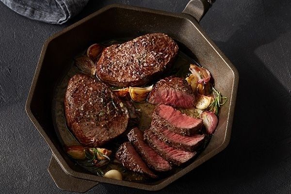 Stekta köttbitar med vitlök och örter i en mörk stekpanna