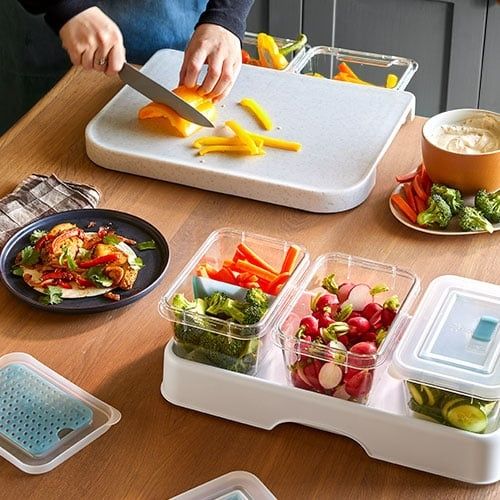 Person skär paprika på en organiserad skärbräda med grönsaker runtomkring