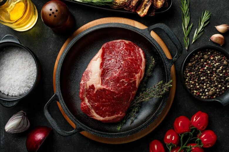 Rå marmorerad köttbit i gjutjärnspanna med örter och kryddor